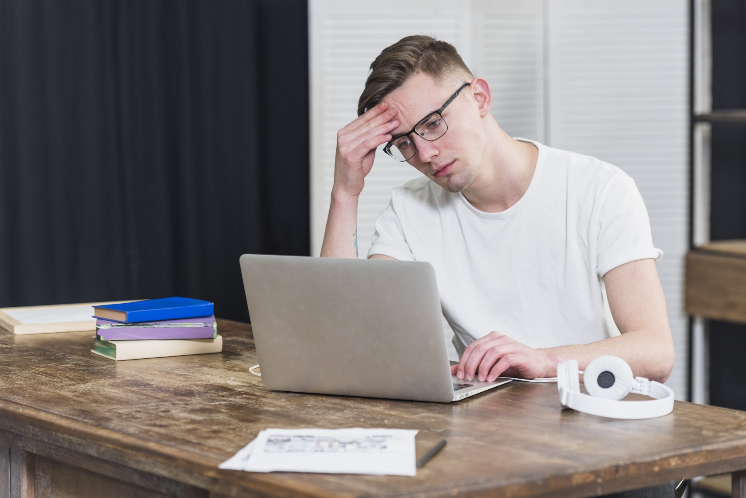 worried-young-man-looking-laptop-wooden-table-min